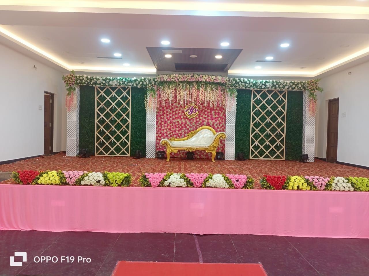 Decorated stage with floral arrangements and a royal chair in an event hall.